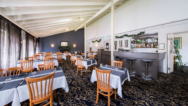 A restaurant with multiple tables and chairs, a bar area, and a patterned carpet. - Burke and Wills Motor Inn (Kingaroy)