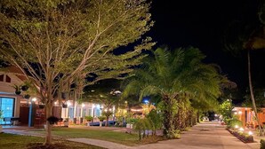 A nighttime view of a resort with a paved walkway, palm trees, and lit buildings. - Saithong Resort (Sikao)