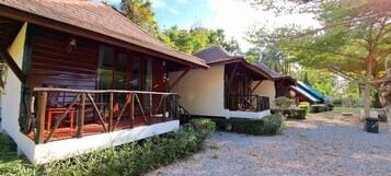 A row of wooden cabins with balconies, surrounded by gravel paths and greenery.