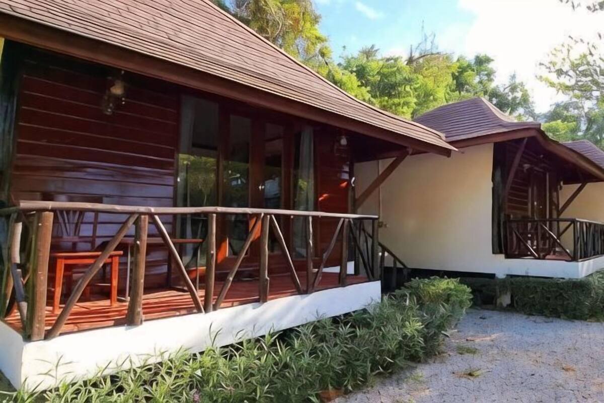 A wooden cabin with a balcony, a covered porch, and a gravel driveway.