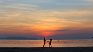 A sunset over a calm body of water with silhouettes of two people holding hands. - Saithong Resort (Sikao)
