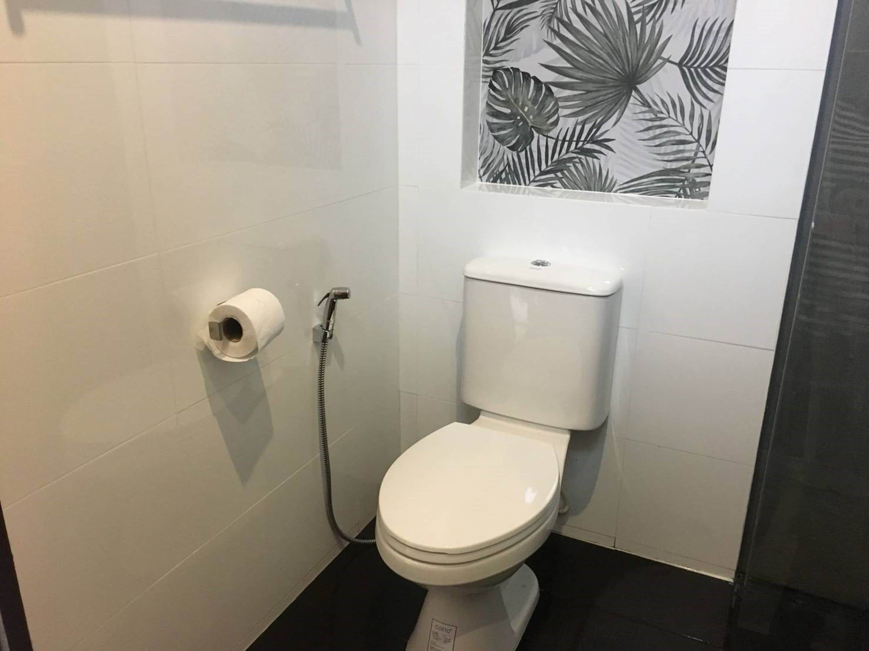 A small, white toilet with a toilet paper holder and a shower head.