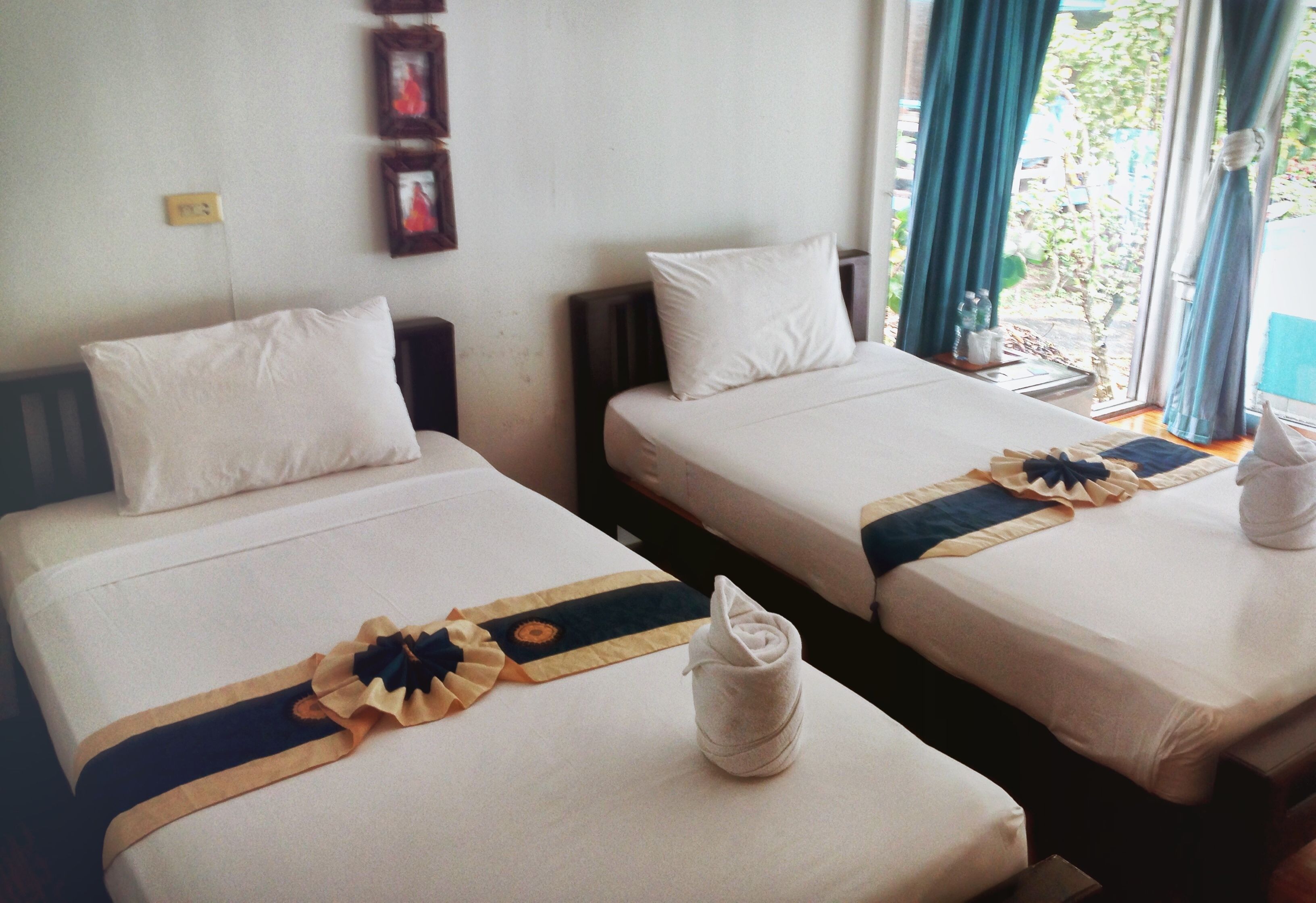 Two twin beds with white linens, a decorative towel, and a blue and gold headboard accent.