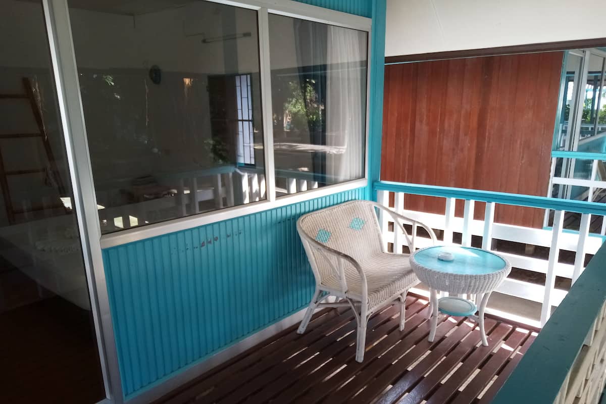 A covered outdoor area with a wicker chair and a small round table, a wooden deck, and a view through a glass door.
