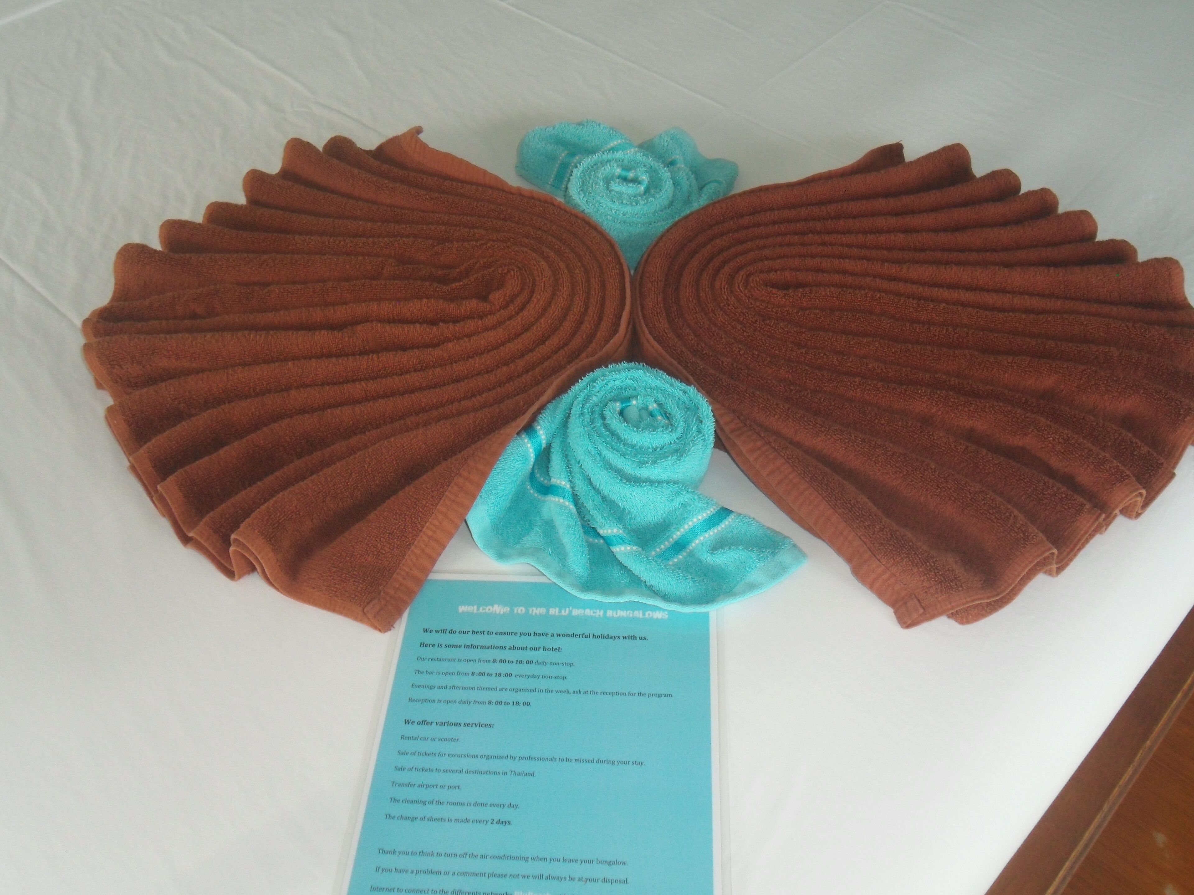 A pair of folded towels arranged in a fan shape on a white surface, with a blue informational card partially visible.
