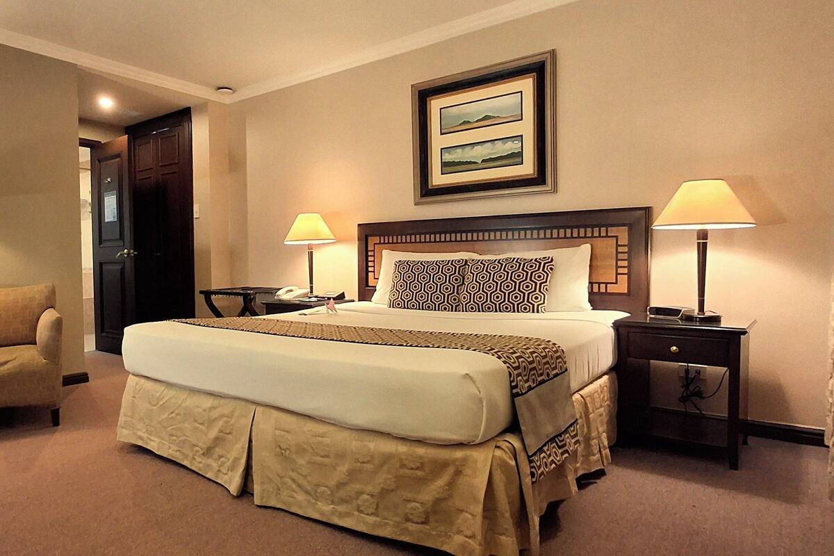 A hotel room with a bed, two bedside tables, a chair, a desk, and a lamp.