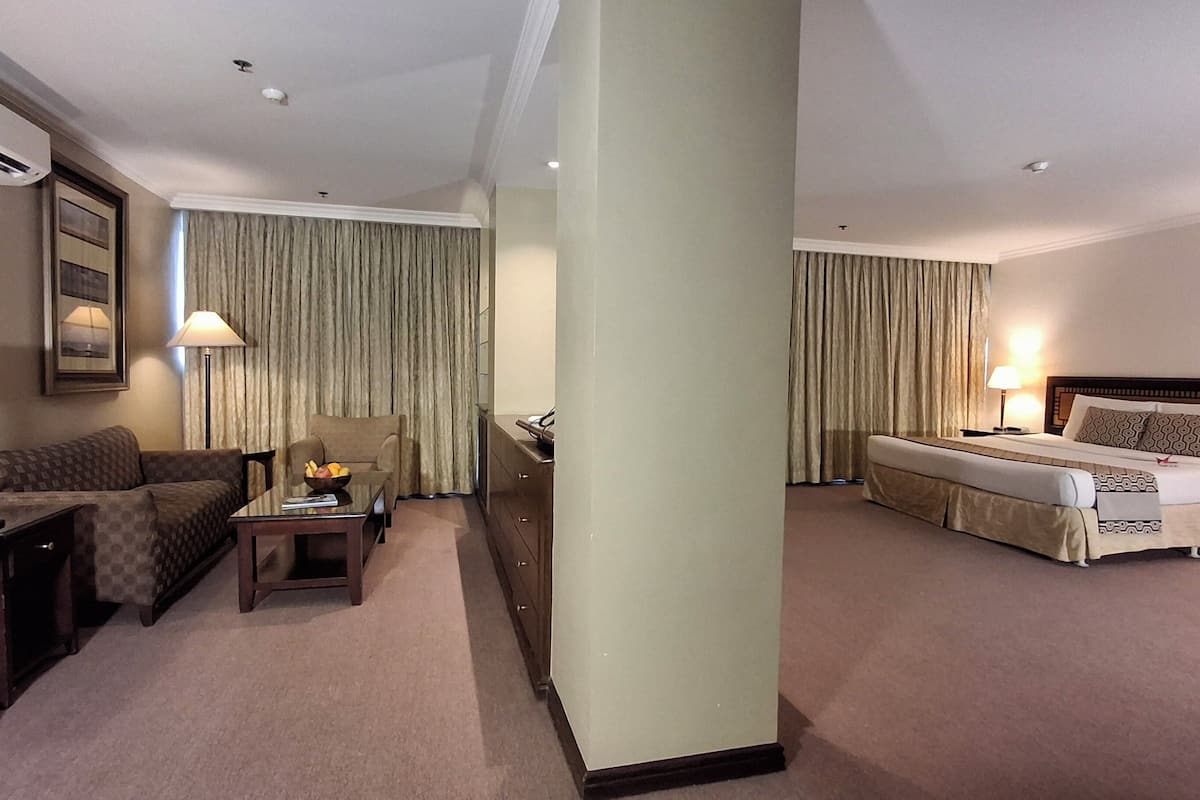 A hotel room with a bed, a sofa, a desk, a lamp, and a chair.