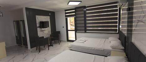 A modern hotel room with two beds, a TV, a desk, and a large window with blinds.