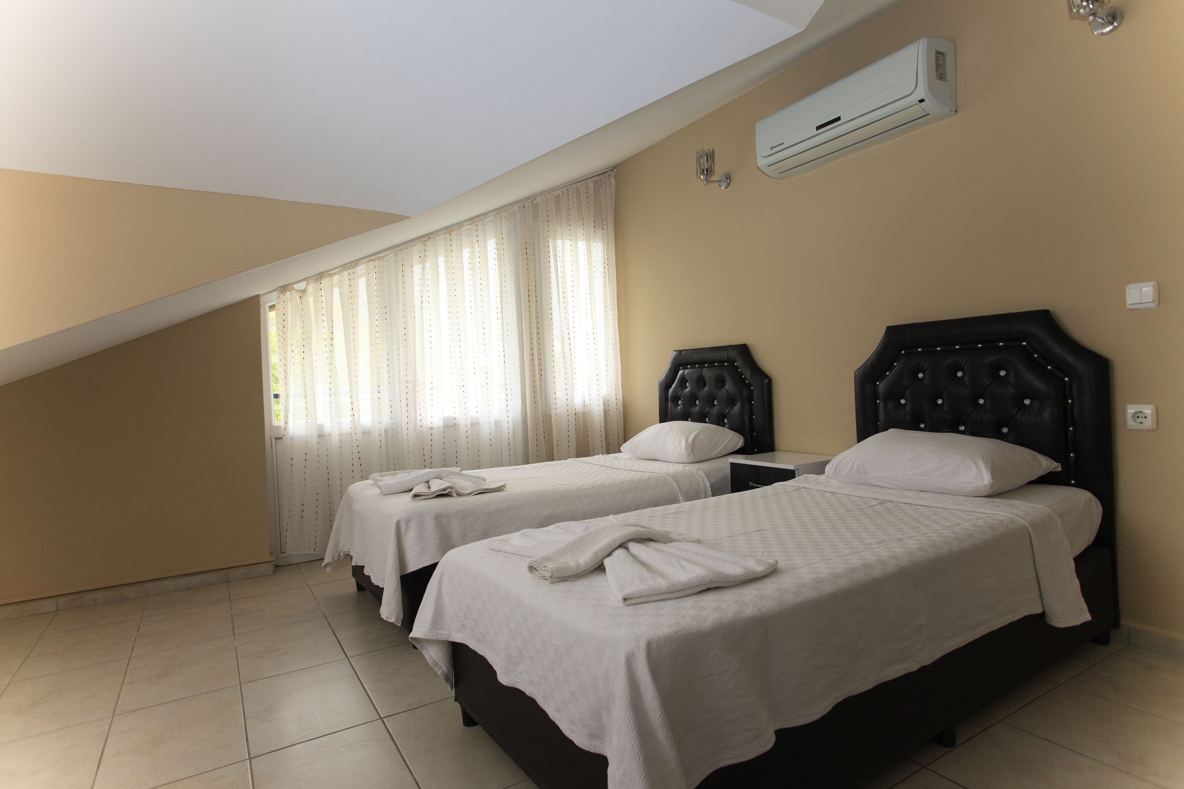A room with two beds, a sloped ceiling, and an air conditioning unit.