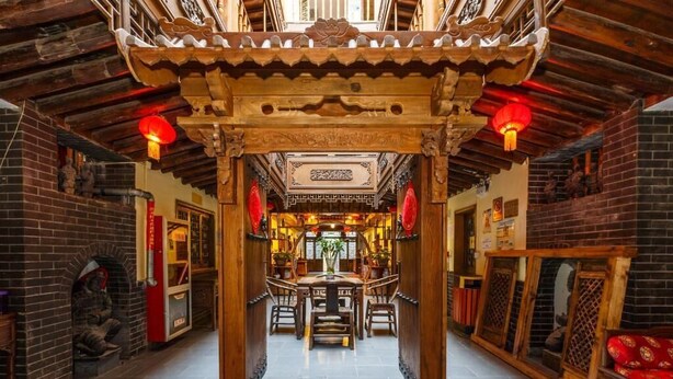 Un corredor de arquitectura tradicional china con un arco de madera, faroles rojos y una mesa central con sillas.