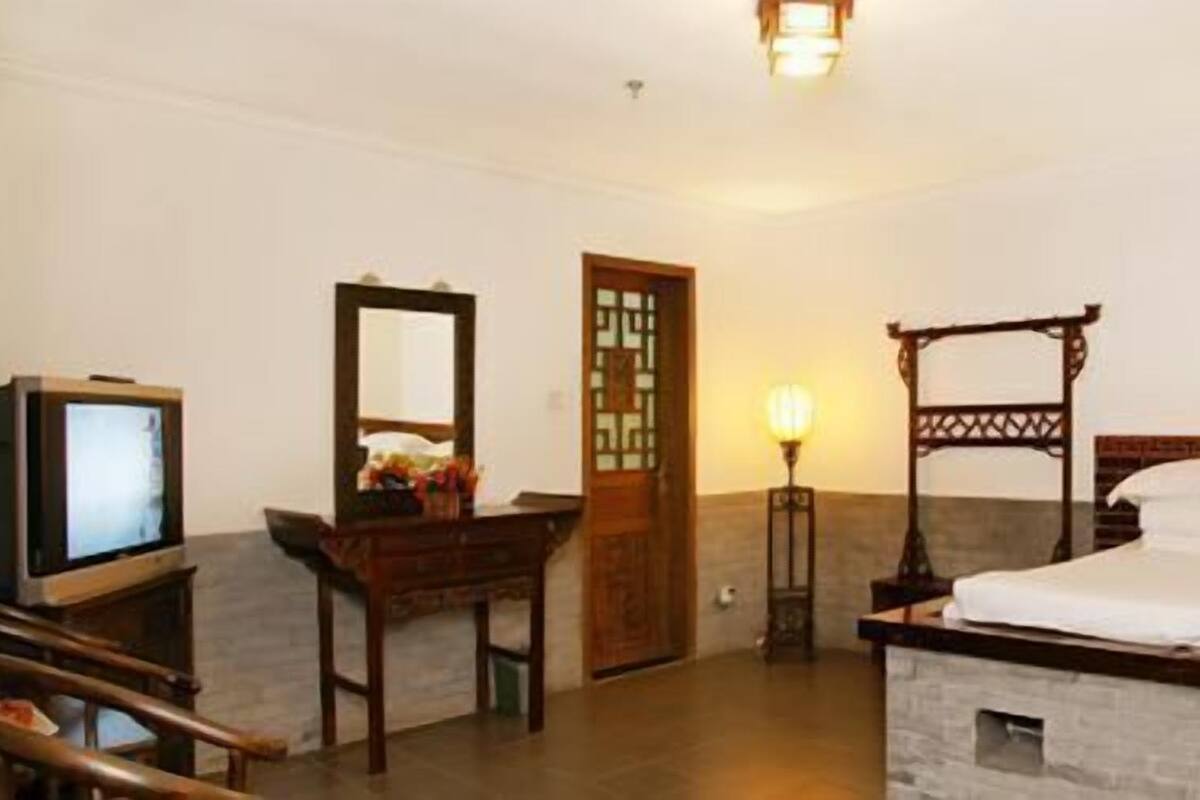 Habitació d'hotel amb llit de fusta, televisor sobre un suport de fusta, escriptori amb cadira i porta amb disseny tradicional.