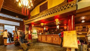 Interior de un restaurante chino tradicional con vigas de madera, faroles rojos y un mostrador de recepción.