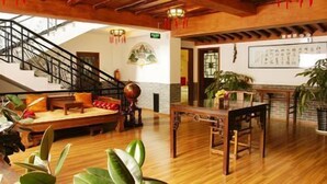 Un vestíbulo amplio con piso de madera, una escalera, una zona de estar con cojines, una mesa con sillas y plantas en macetas.