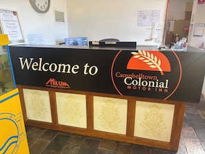 A reception desk with a sign welcoming guests to Campbelltown Colonial Motor Inn, part of the Milum Group Hotels.