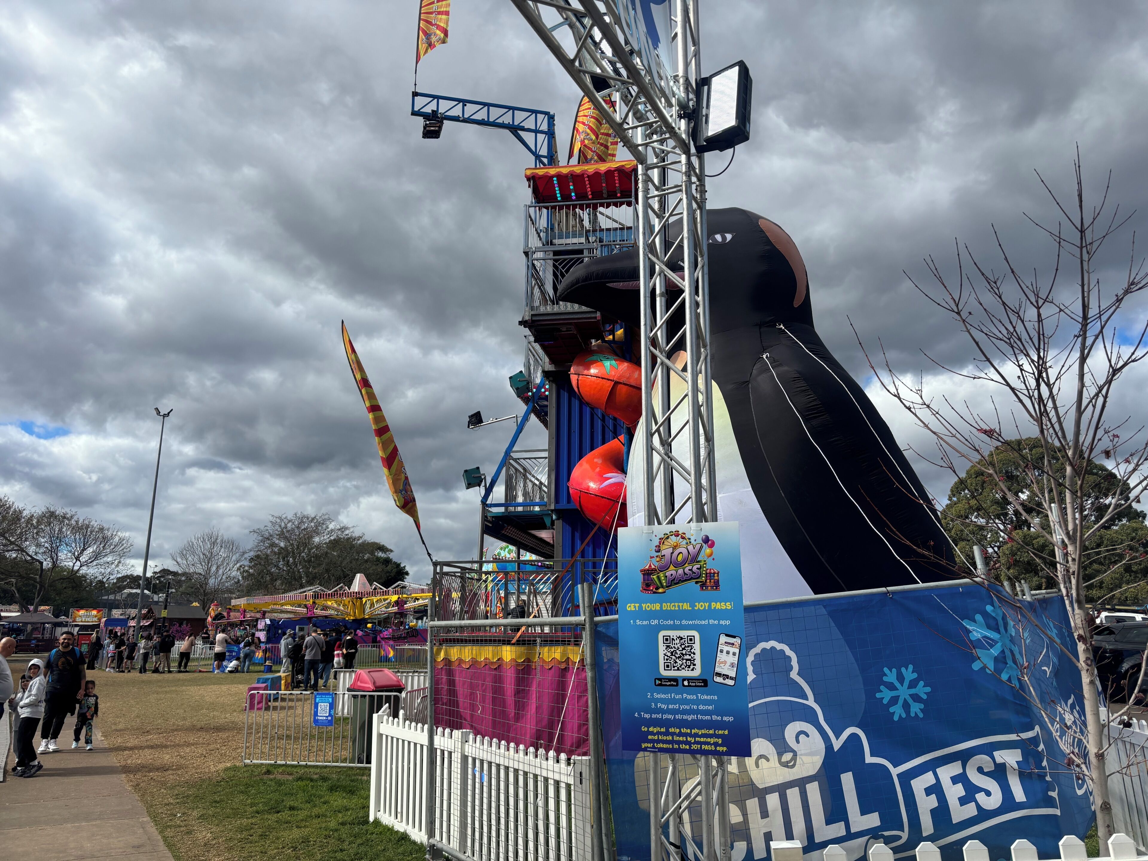 Une attraction de fête foraine avec une grande structure noire et rouge, une banderole bleue portant l'inscription « CHILL FEST » et un code QR pour un pass numérique.