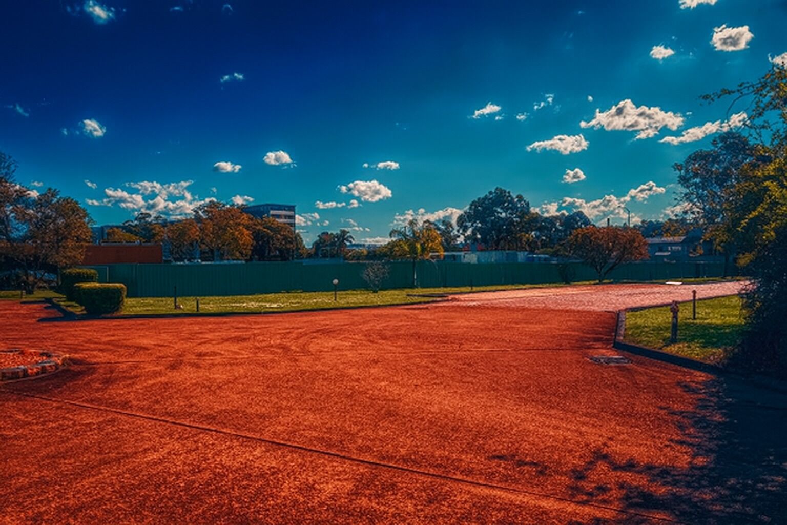 Ein Tennisplatz mit grünem Zaun, Bäumen und blauem Himmel.