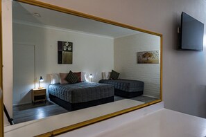 Une chambre avec un grand miroir, deux lits, une table de chevet avec une lampe et des œuvres d’art accrochées au mur.