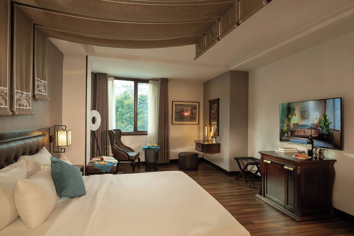 Une chambre d’hôtel avec un grand lit, un bureau avec une chaise, une télévision et une fenêtre avec des rideaux.