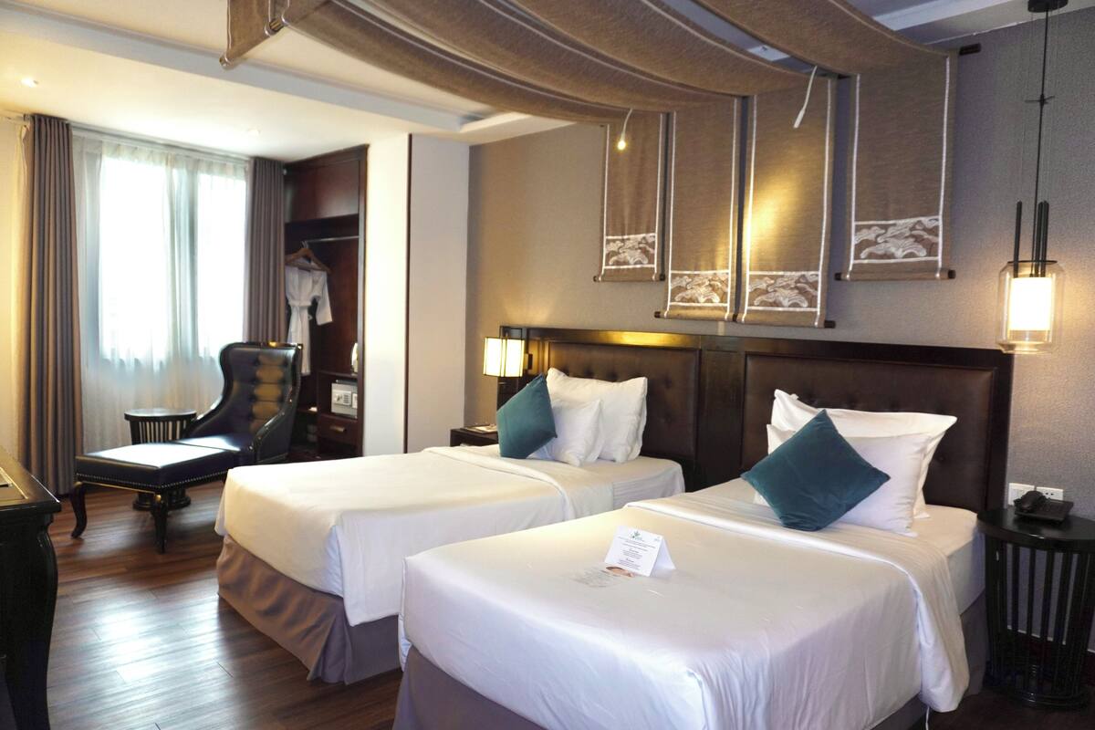 Une chambre d’hôtel avec deux lits, un bureau, une chaise et une armoire.