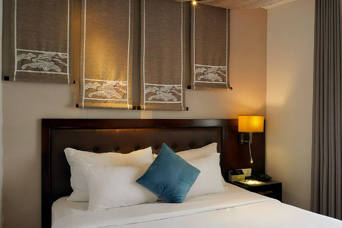 Une chambre d’hôtel avec un grand lit, une tête de lit, une table de chevet avec une lampe et un mur orné de panneaux décoratifs.