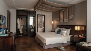 A hotel room with a large bed, a desk with a chair, a wardrobe, a mirror, and a bedside table with a lamp.