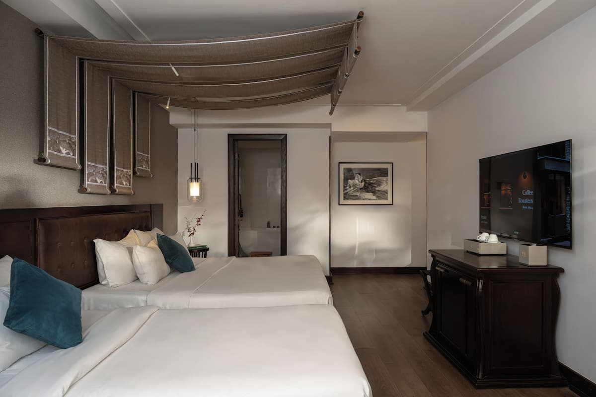 Une chambre d’hôtel avec deux lits, une télévision, une armoire et un tableau encadré au mur.