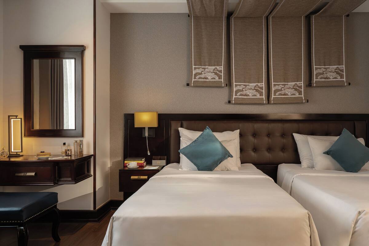 Une chambre d’hôtel avec deux lits, un grand miroir, un bureau avec une lampe et une table de chevet avec une lampe.