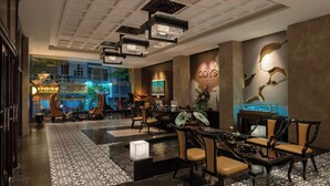 A hotel lobby with a reception desk, seating area, and a large window overlooking the street.