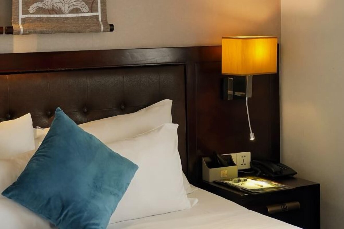 A neatly made bed with white and blue pillows, a dark headboard, and a bedside table with a lamp, phone, and a small box.