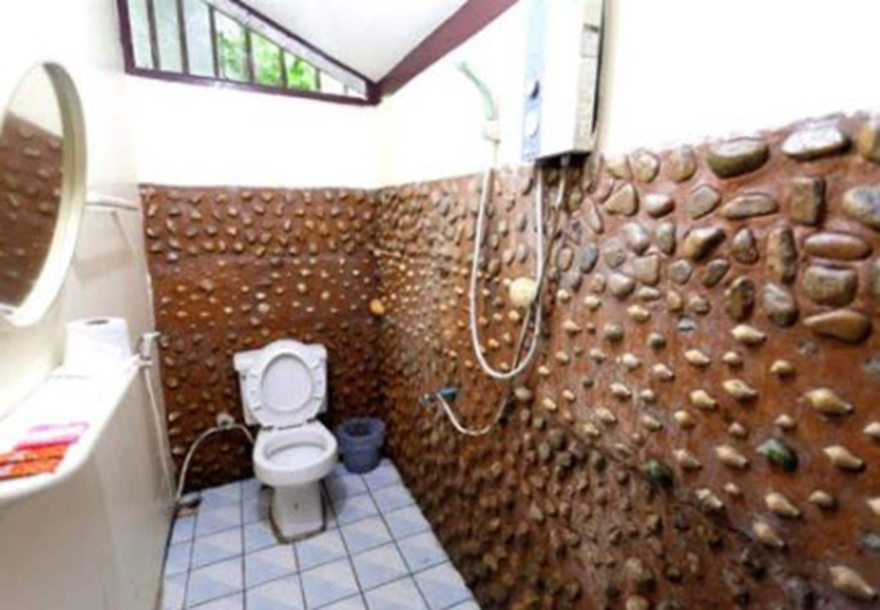A bathroom with a toilet, a sink, and a shower. The walls are covered with a textured stone-like material.