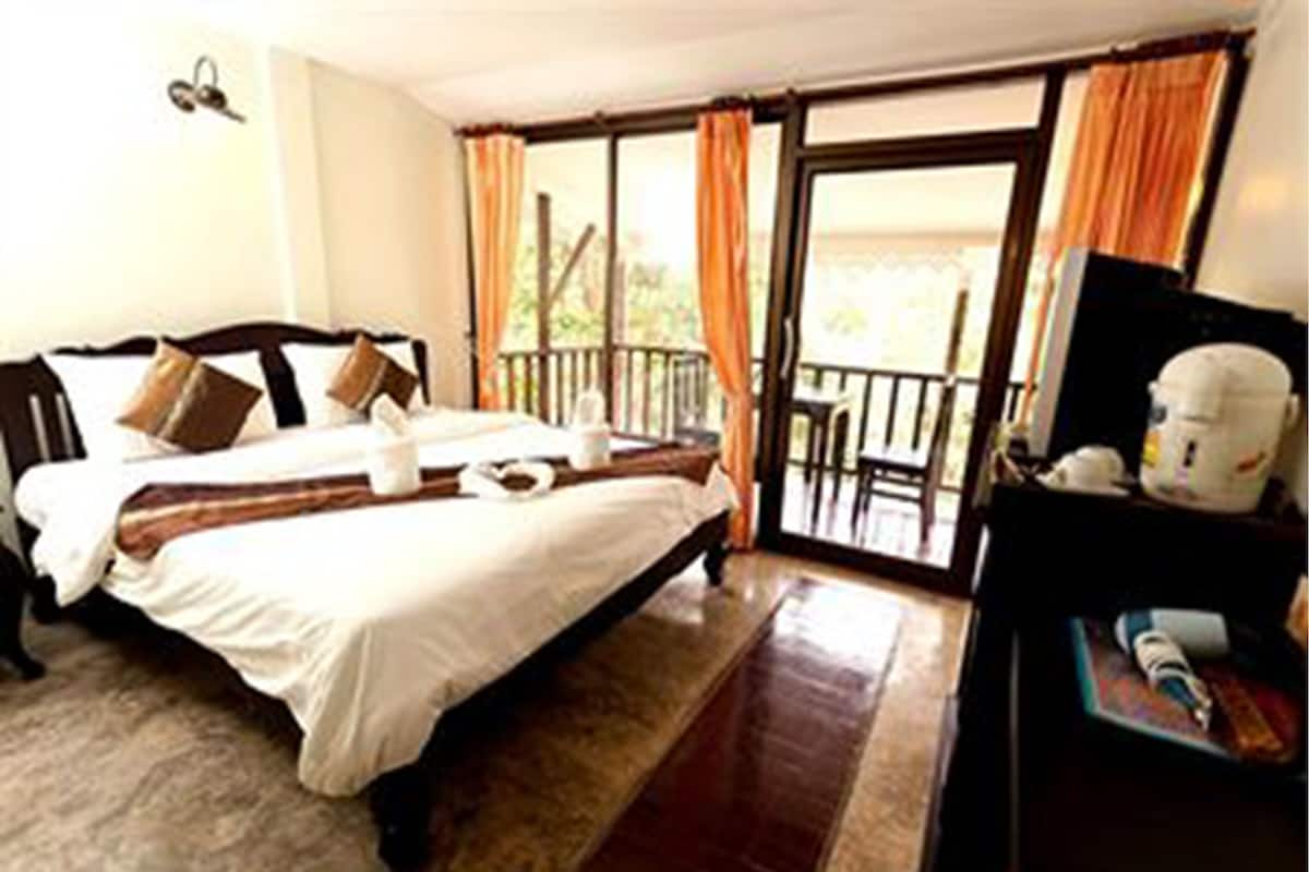 A hotel room with a large bed, a desk with a computer, and a balcony with orange curtains.