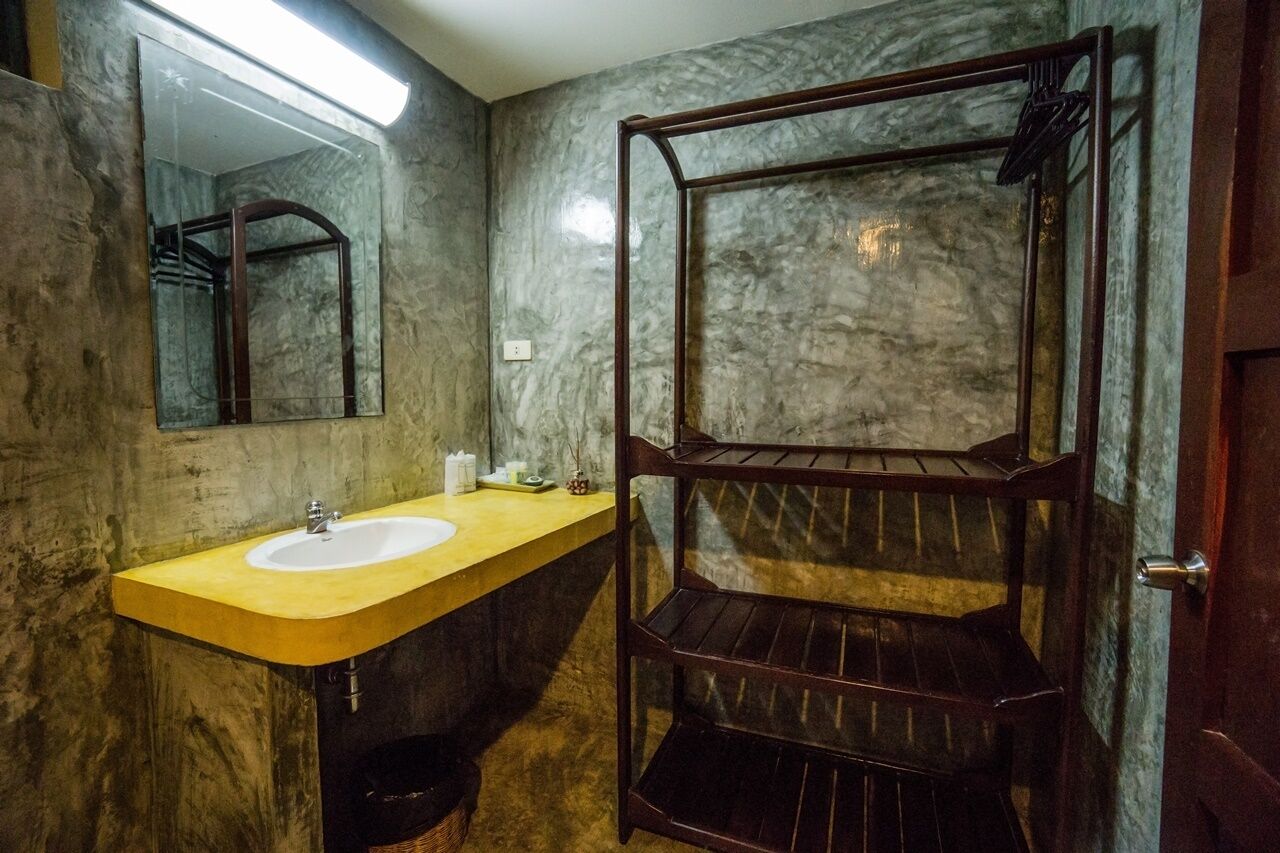 A bathroom with a marble wall, a sink, a mirror, and a wooden shelf.