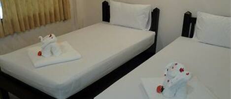 Two single beds with white linens and headboards, a window with beige curtains, and a small table with a white cloth and a red object.