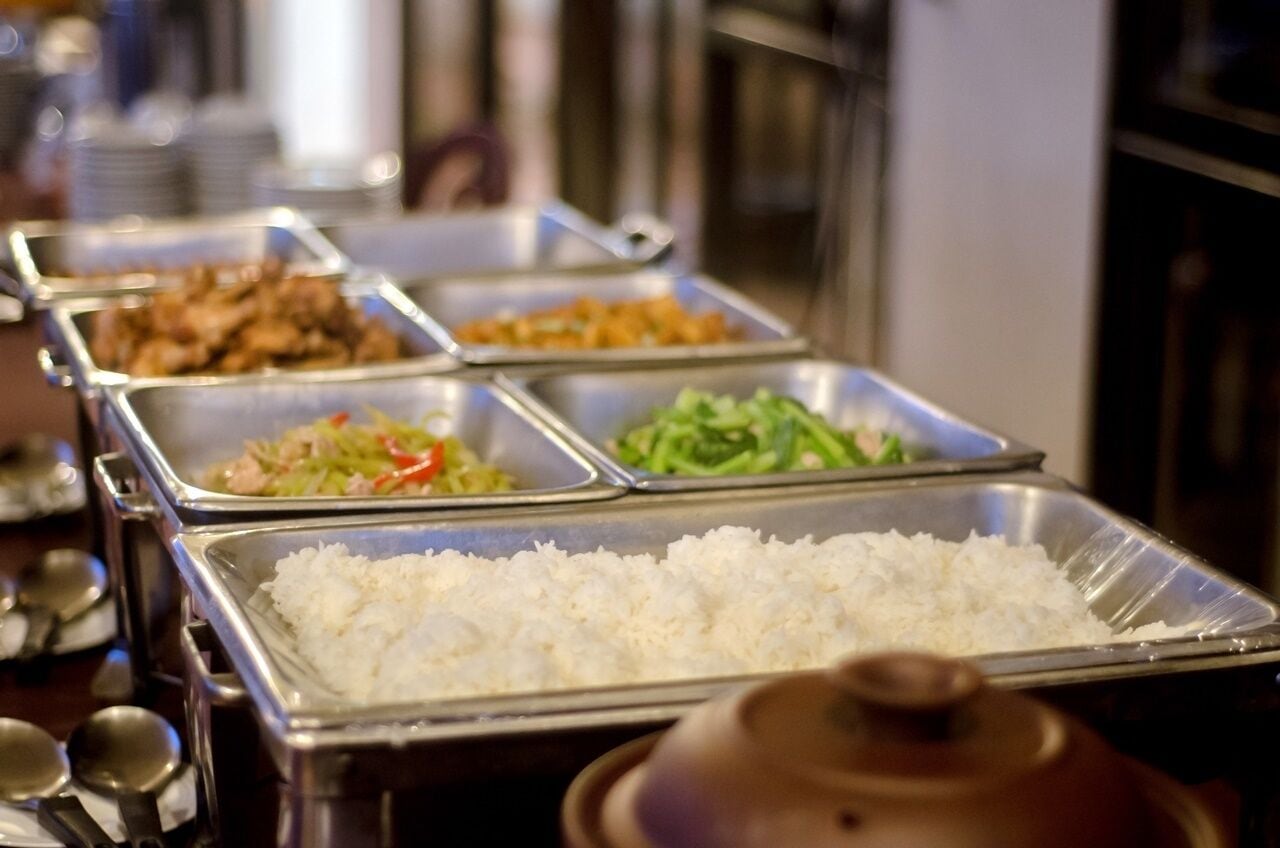 A buffet with multiple food trays, including rice, vegetables, and meat dishes.