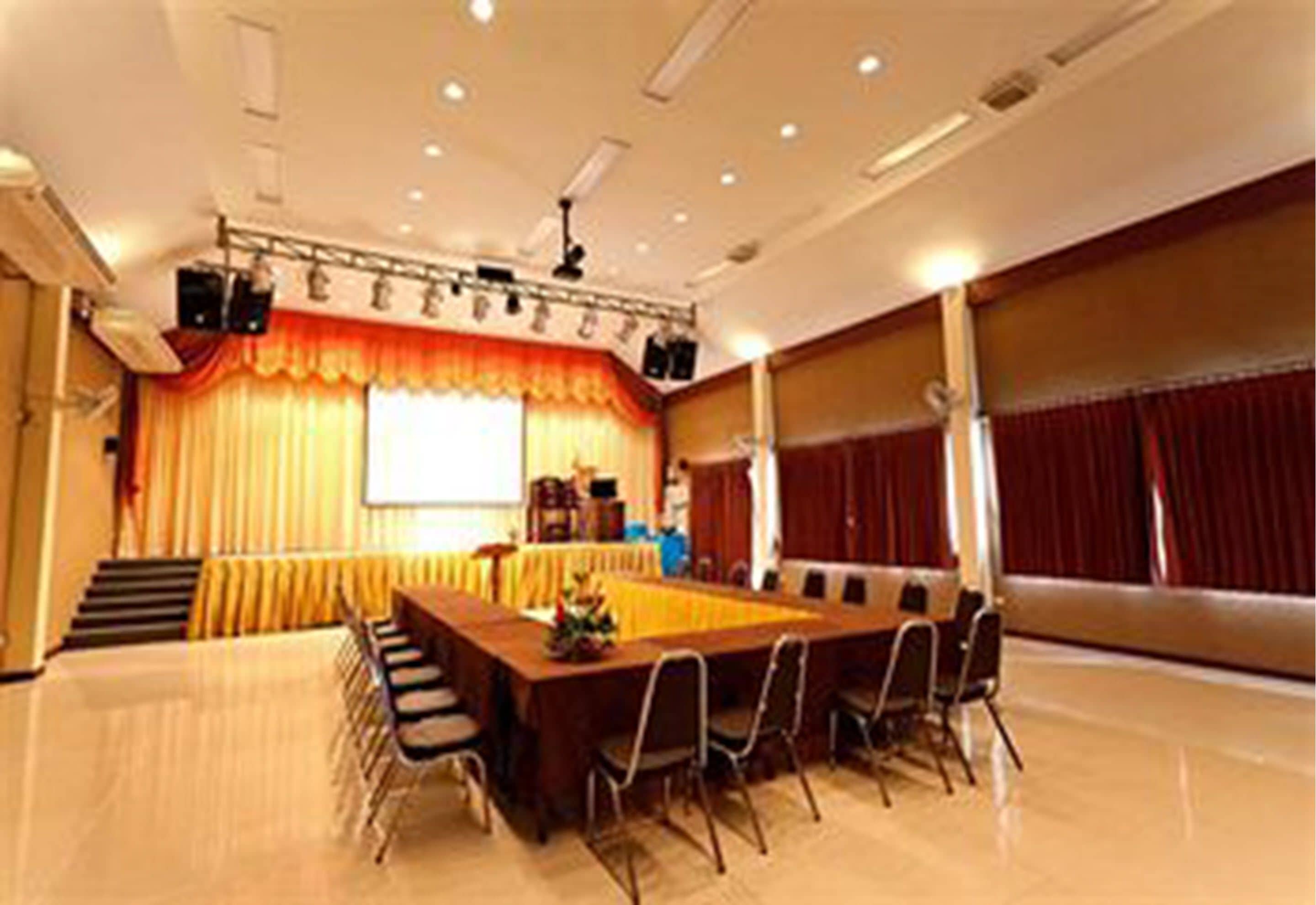 A conference room with a long table, chairs, a projector screen, and a stage with curtains.