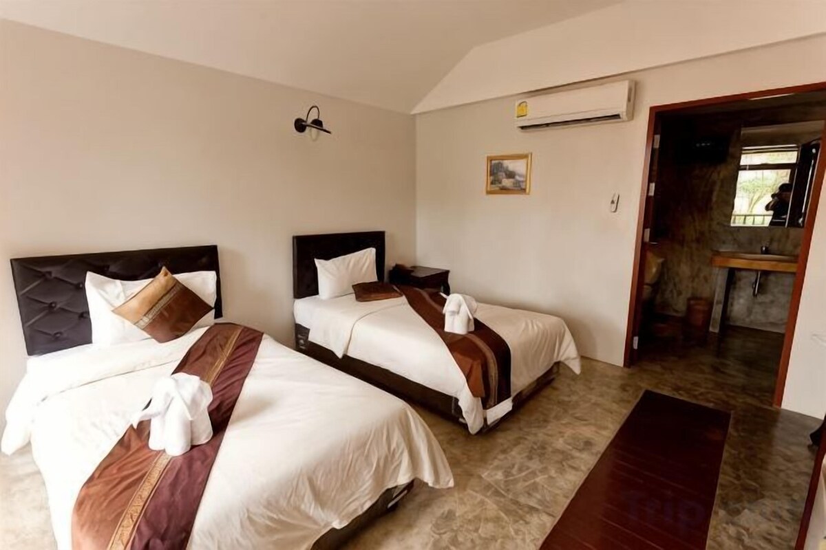 A hotel room with two beds, a wooden bench, a wall-mounted air conditioner, and a door leading to a bathroom.