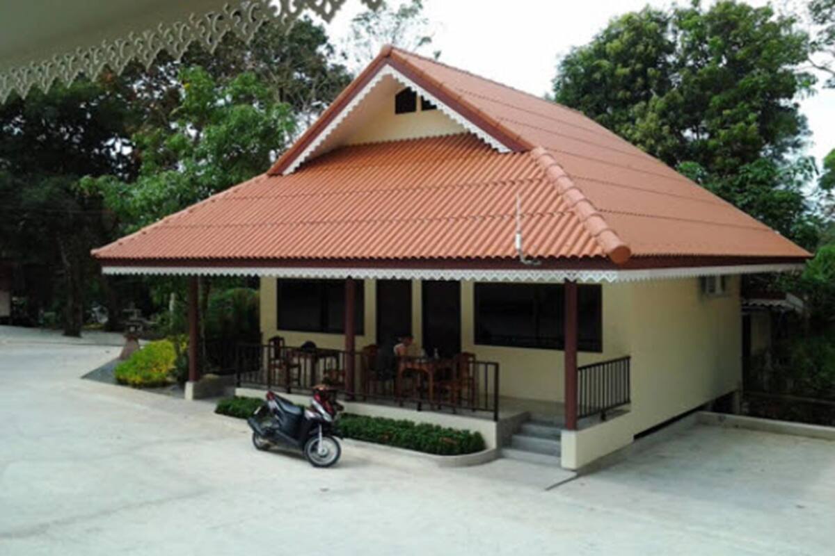 A single-story building with a tiled roof, a porch with chairs, and a motorcycle parked in front.