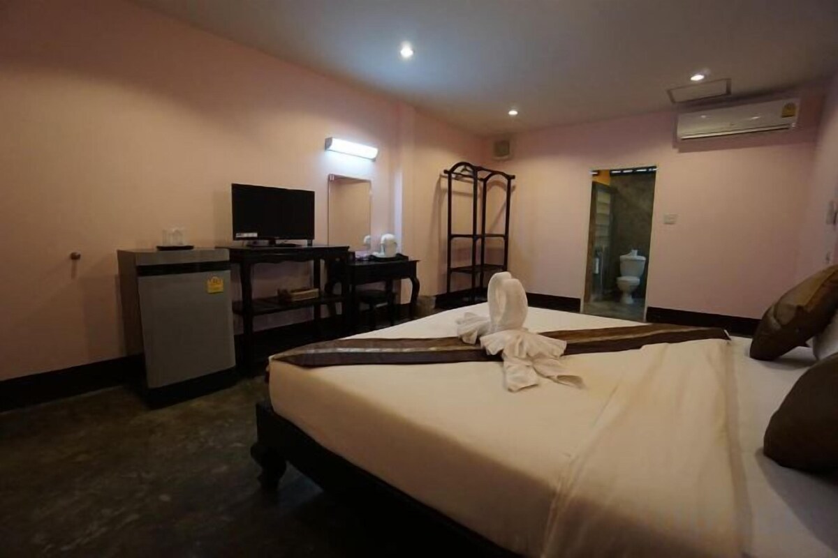 A hotel room with a bed, a desk with a television, a small refrigerator, and a mirror.