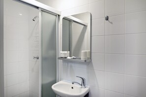 Uma casa de banho com cabine de duche em vidro, lavatório branco com torneira cromada e espelho sobre o lavatório.