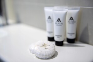 Um banheiro com pia branca, um saboneteira e três frascos de sabonete Alveda.