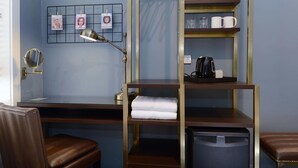 A hotel room with a desk, a chair, a shelf with towels, a coffee maker, and a trash bin. - The Maisonette (Potts Point)