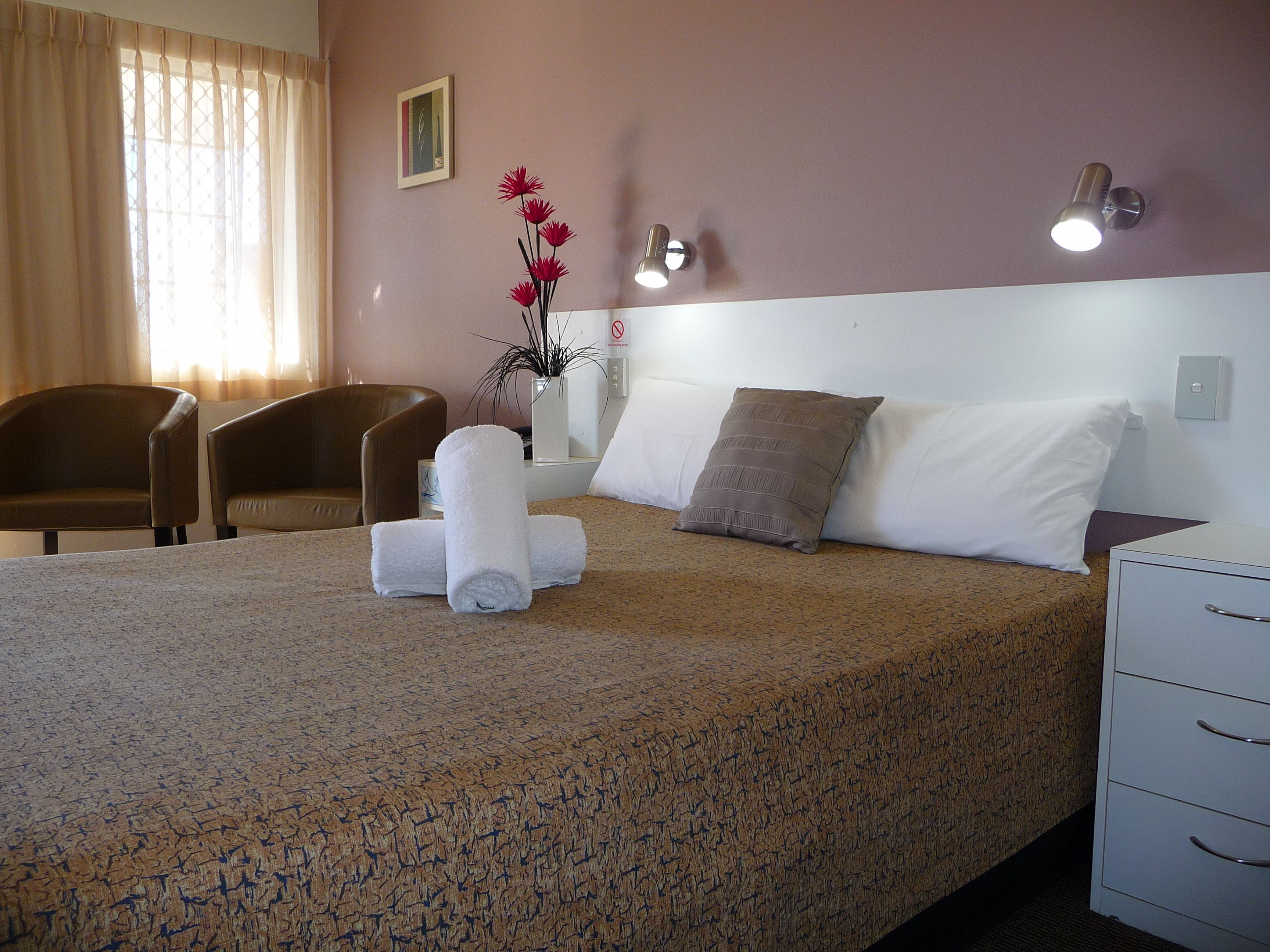 Une chambre d’hôtel comprenant un lit, une chaise, une table de chevet et un luminaire fixé au mur.