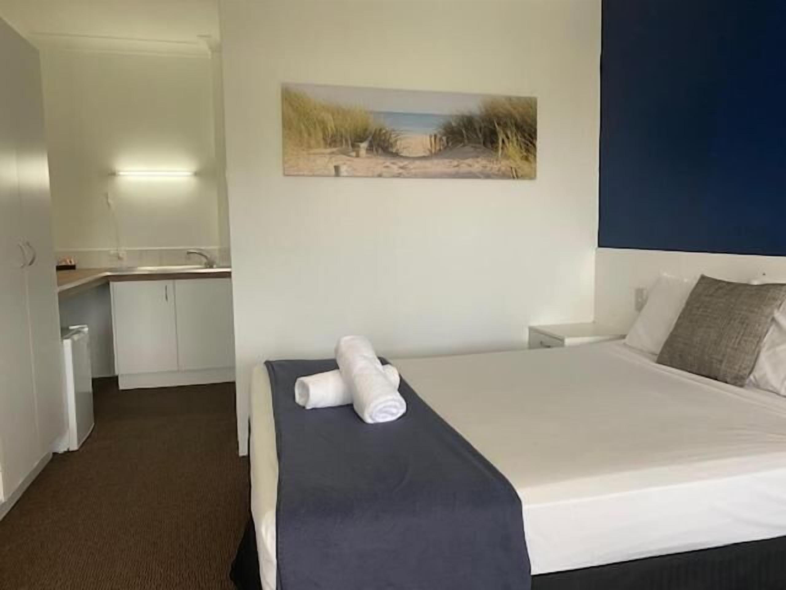A hotel room with a bed, a desk, and a painting of a beach scene.