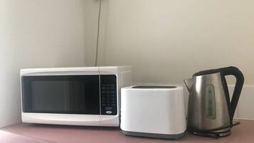 Un microondas, un tostador y una tetera sobre una encimera rosa.