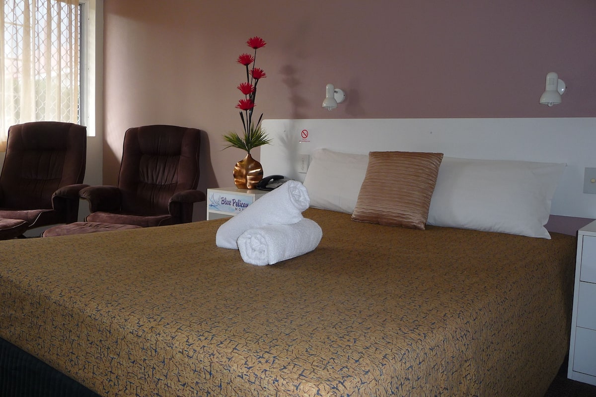 A hotel room with a bed, two armchairs, a small table with a vase and a telephone, and a sign indicating the room type.