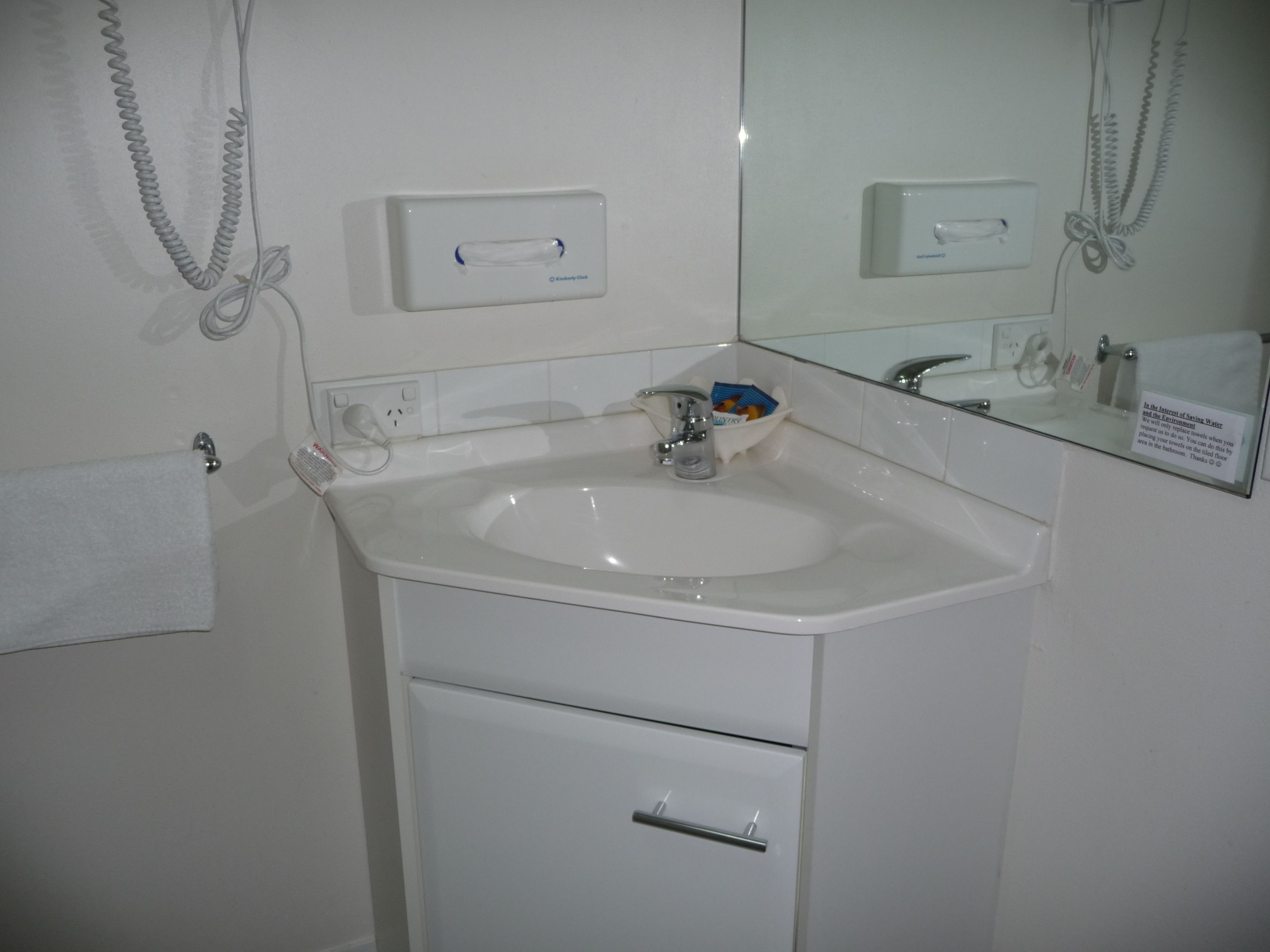 Ein Badezimmer mit einem weißen Waschbecken, einem Spiegel, einem Handtuchhalter und einer Seifenspender.