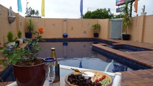 A poolside setting with a table holding a wine glass, a bottle, and a fruit platter. - Blue Pelican Motel (Tweed Heads)