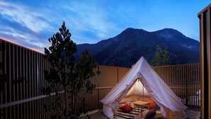 Un hébergement sous tente offrant une vue sur les montagnes, avec une terrasse en bois et une petite table agrémentée de coussins.