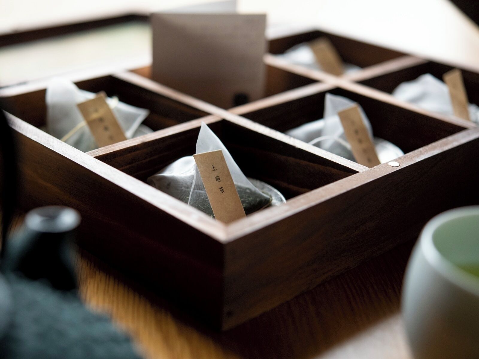 Una caja de madera con compartimentos, cada uno conteniendo una bolsita de té con una etiqueta.