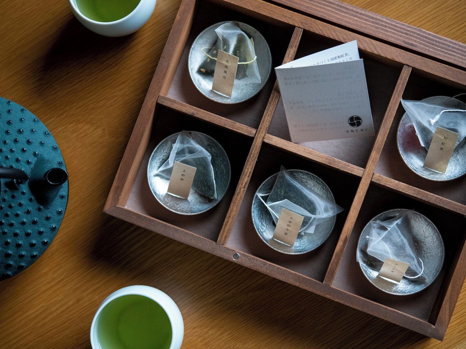 Una bandeja de madera con seis compartimentos que contienen bolsitas de té y una tarjeta.